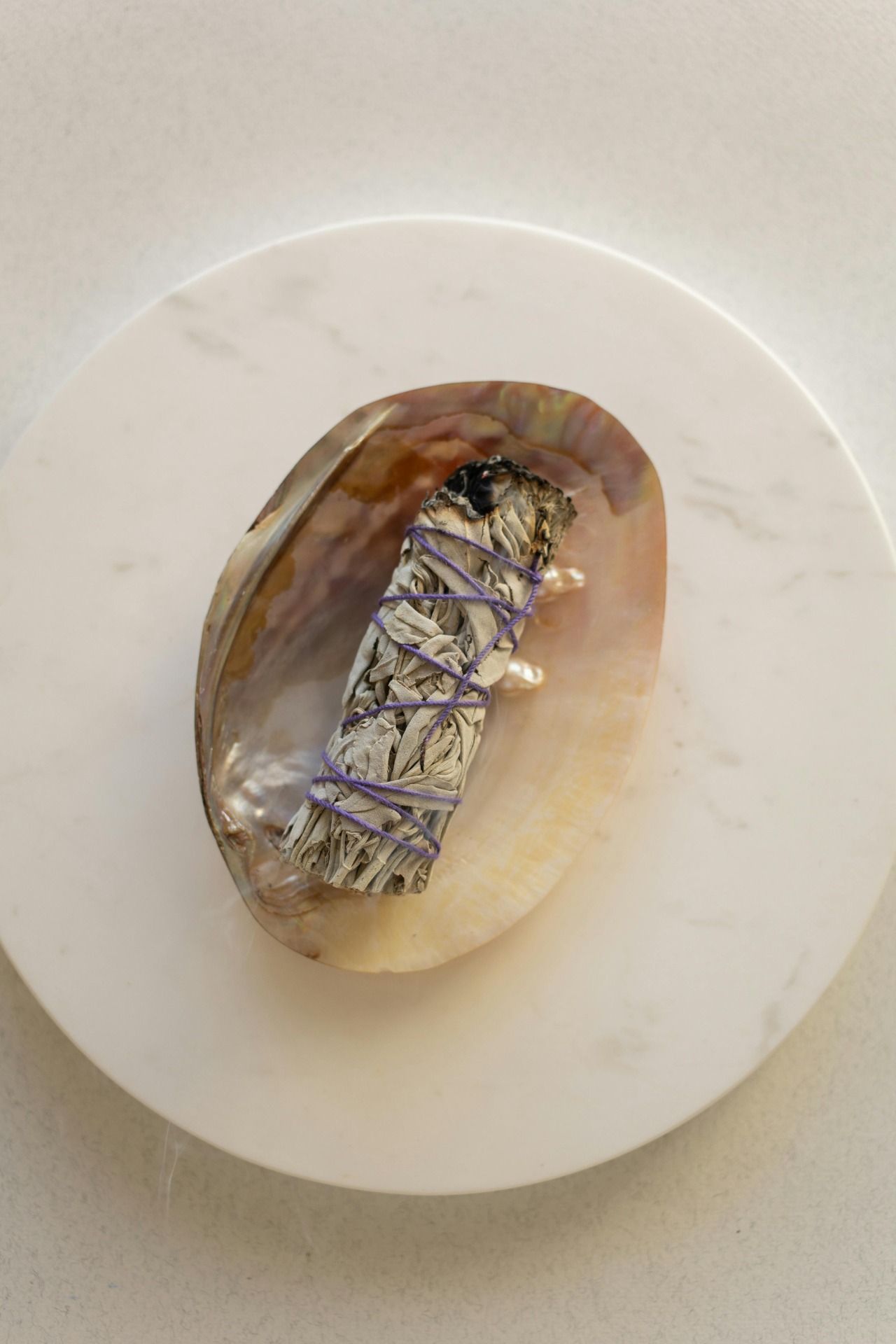 Witte schaal met ingepakte salie-achtige bundel, vastgebonden met paarse draad en zwarte kern.
